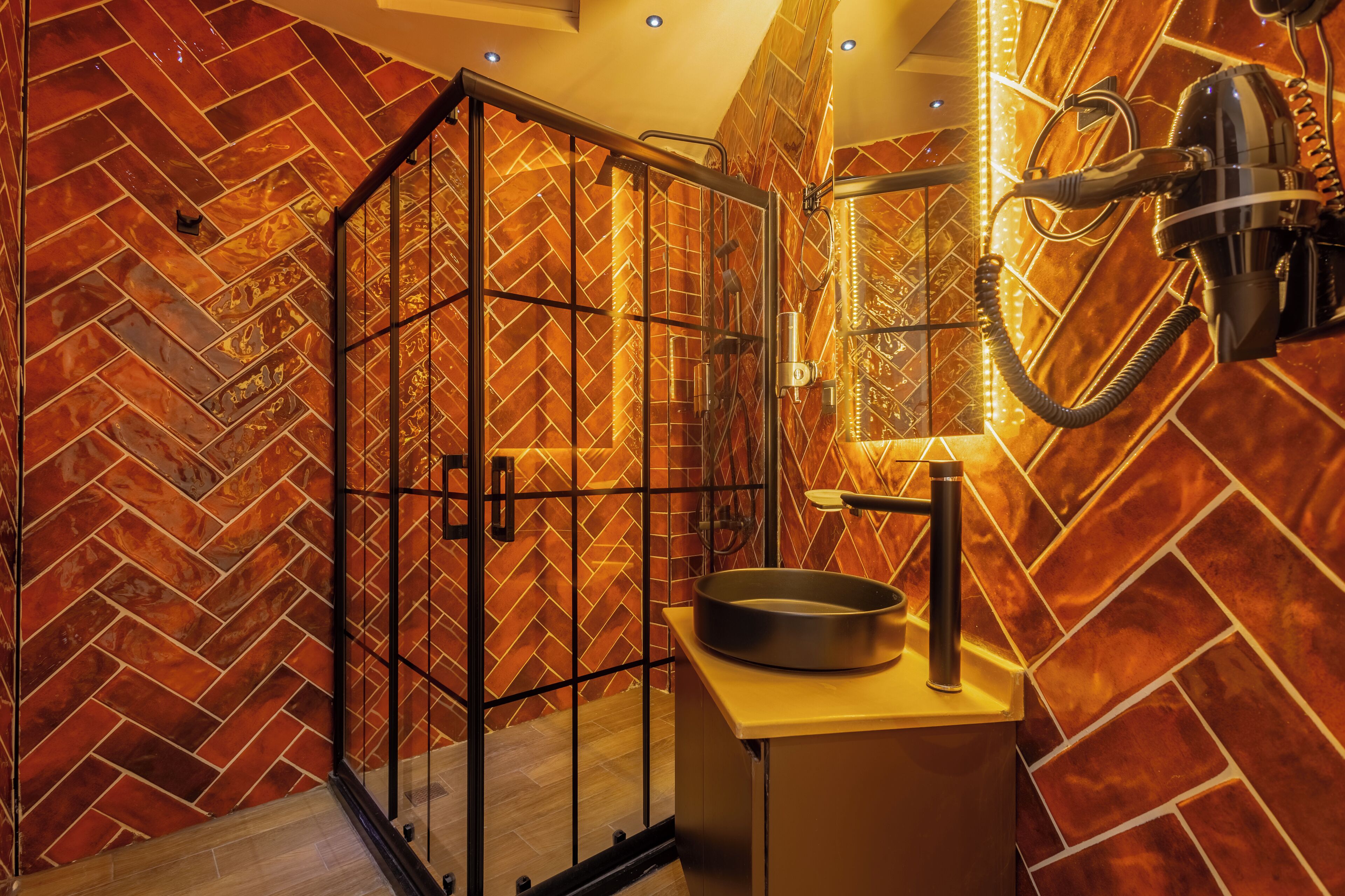 Un baño moderno con pared de azulejos en patrón de espiga, cabina de ducha de vidrio y lavabo redondo con ducha de mano.
