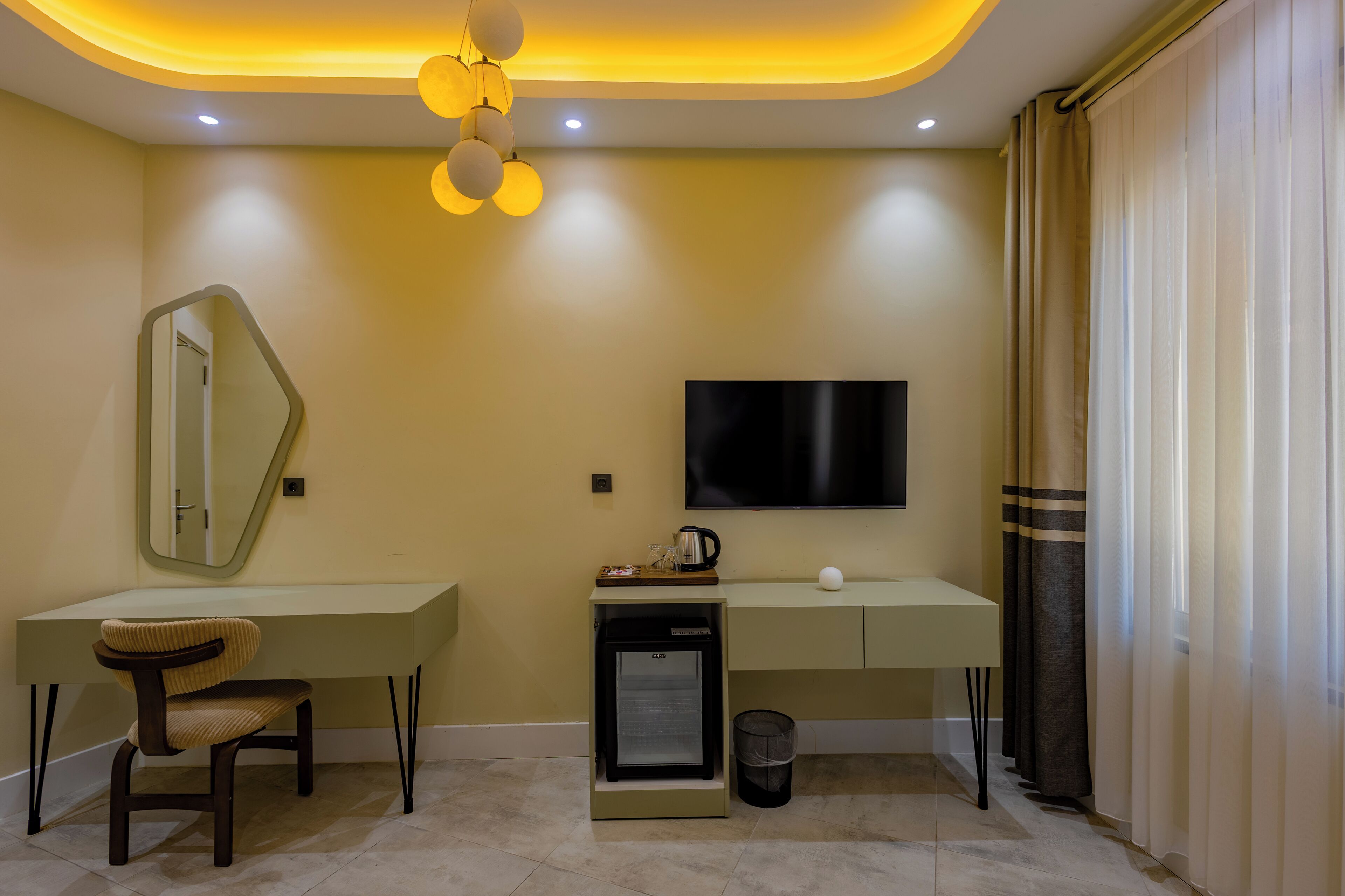 A modern hotel room with a desk, chair, TV, and a small refrigerator.