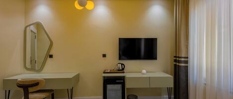 A modern hotel room with a desk, chair, TV, and a small refrigerator.