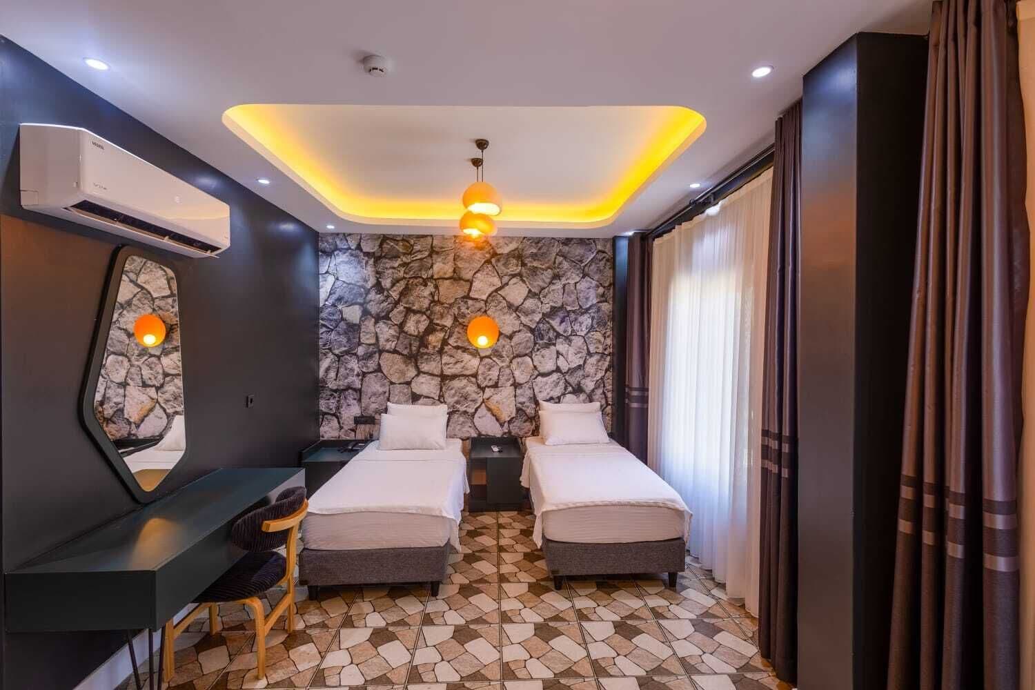 Una habitación de hotel moderna con dos camas, un escritorio y una pared de piedra.