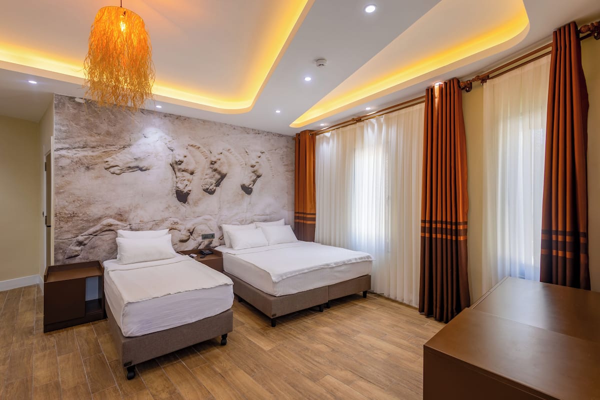 A hotel room with two beds, a marble wall, a modern chandelier, and a large window with curtains.