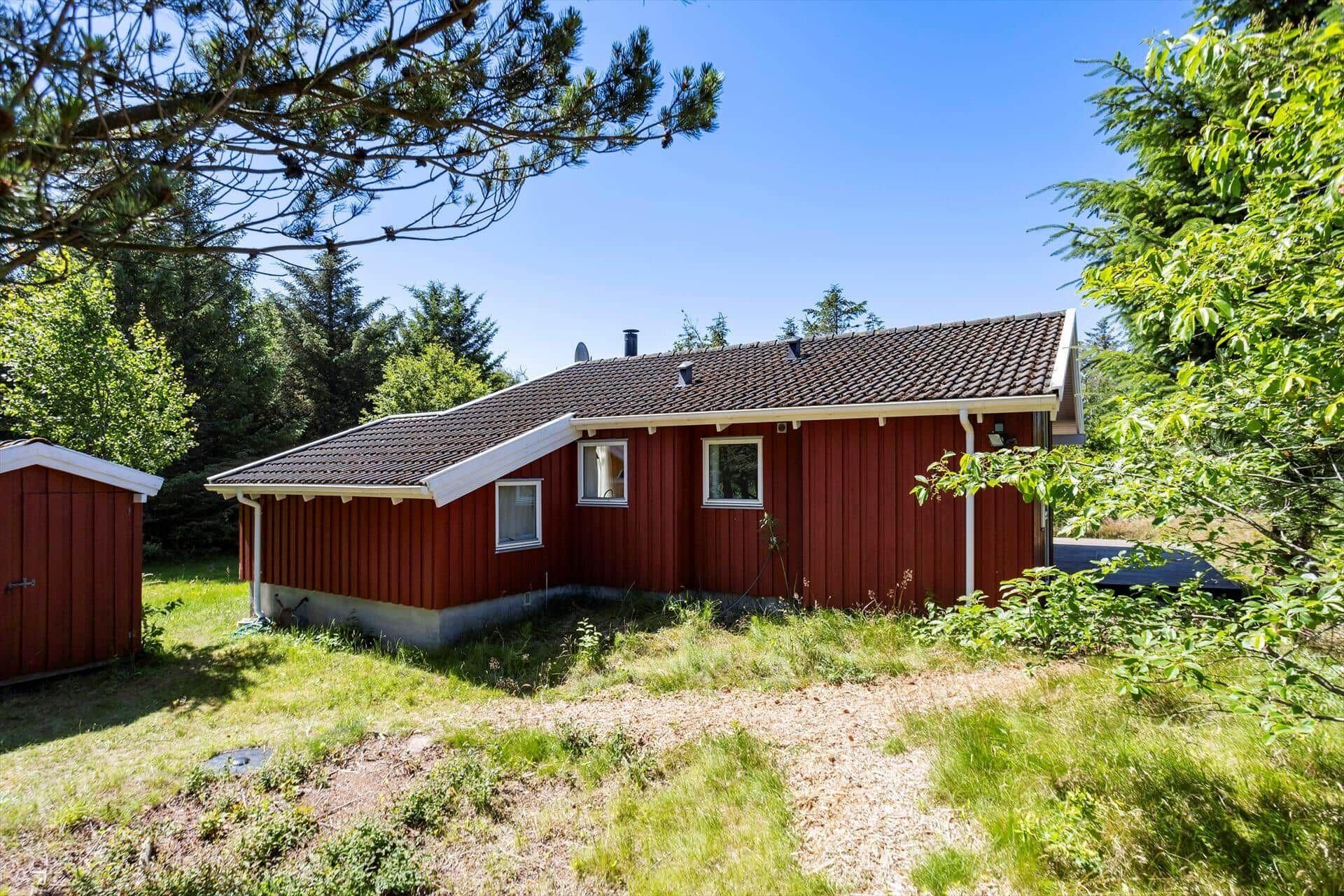 Eine rote Holzhütte mit Ziegeldach, umgeben von Grünpflanzen und Bäumen.
