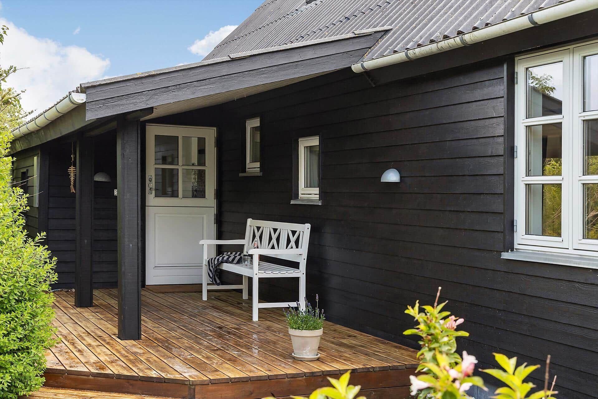 A dark wooden house with a porch, a white bench, and a door with glass panels.