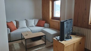 Una habitación acogedora con un sofá, una mesita de centro y un televisor sobre un soporte de madera.