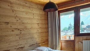 Un dormitorio de cabaña de madera con una cama, una lámpara colgante y una ventana con vistas a edificios.