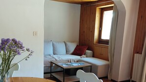 Una sala de estar acogedora con techo de madera, un sofá, una mesa de centro y una mesa de comedor con sillas.