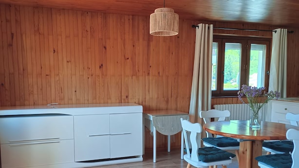 Una habitación con paneles de madera, una mesa de comedor con sillas, un banco y una lámpara colgante.