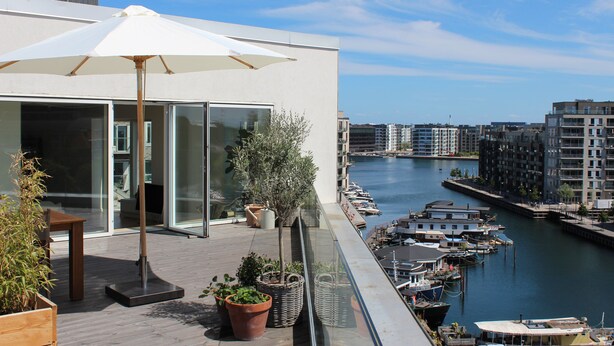 A modern building with a glass facade overlooking a marina with boats. - Modern penthouse w. canal view and private rooftop terrace, 10min to city center (København)