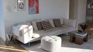 A modern living room with a sofa, ottoman, glass coffee table, and artwork on the wall. - Modern penthouse w. canal view and private rooftop terrace, 10min to city center (København)