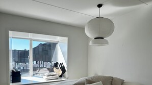 A bedroom with a large bed, a window with a view of buildings, a radiator, and a hanging light fixture. - Modern penthouse w. canal view and private rooftop terrace, 10min to city center (København)