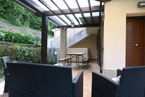 An outdoor patio with wicker furniture, a wooden table, and a staircase leading to an upper level.