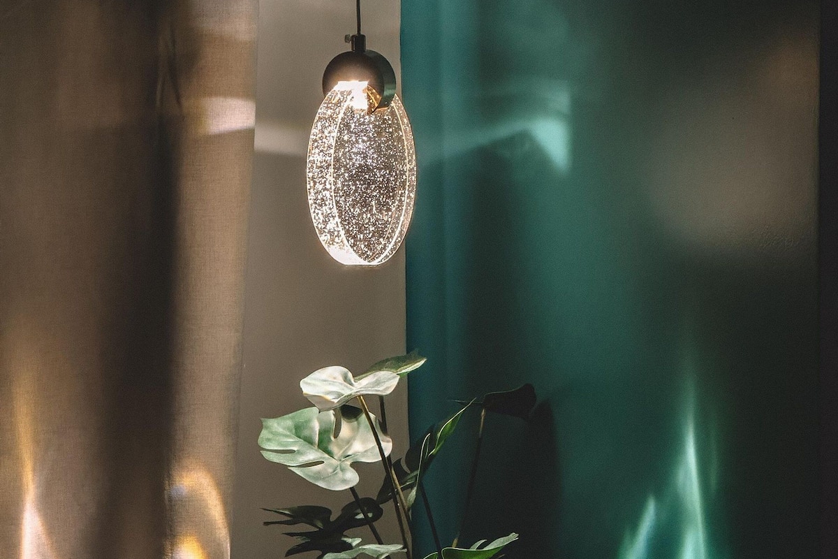 A room with a hanging light fixture, a potted plant, and a teal curtain.