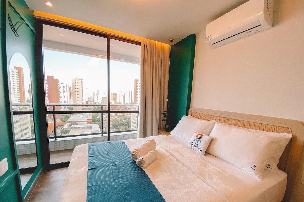 A hotel room with a bed, a window with a city view, and an air conditioning unit.