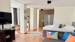 A modern living room with a flat-screen TV, a sofa, a coffee table, and a bed with colorful pillows. - Exclusive flat, front row, directly on the beach, 200m from the pier (Binz)