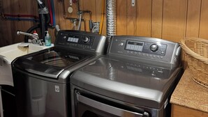 Une buanderie équipée de deux machines à laver à chargement frontal, d’un sèche-linge et d’une étagère contenant des produits de nettoyage.