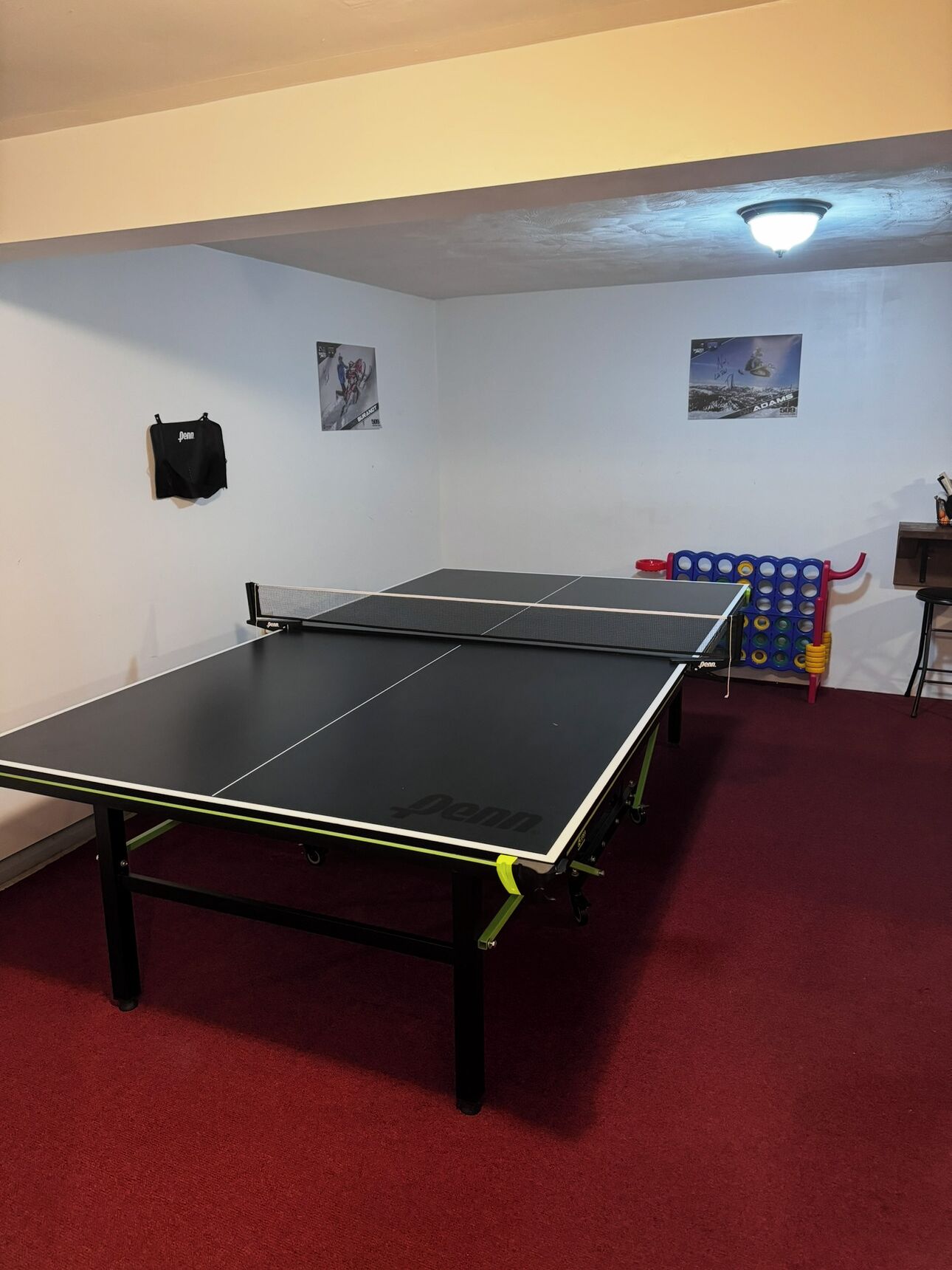A room with two ping pong tables, a red carpet, and a ceiling light fixture.