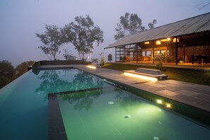 A swimming pool with a stone deck, a covered seating area, and a stone building with a metal roof. - VAASTA Vagamon (Peermade)