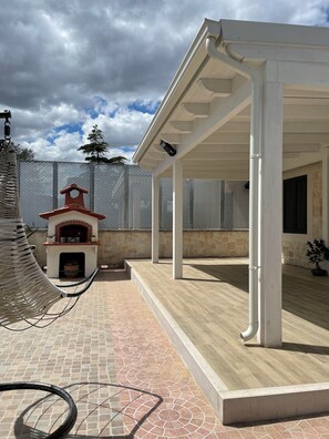 Un patio couvert doté d’une cheminée en pierre, d’une pergola et d’un espace extérieur clos.