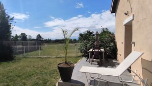 Une terrasse avec une table et des chaises, un pot de fleurs et, au fond, une zone délimitée par une clôture.