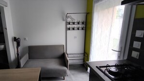 Une cuisine compacte avec un canapé gris, un porte-manteau suspendu et une fenêtre ornée de rideaux légers.