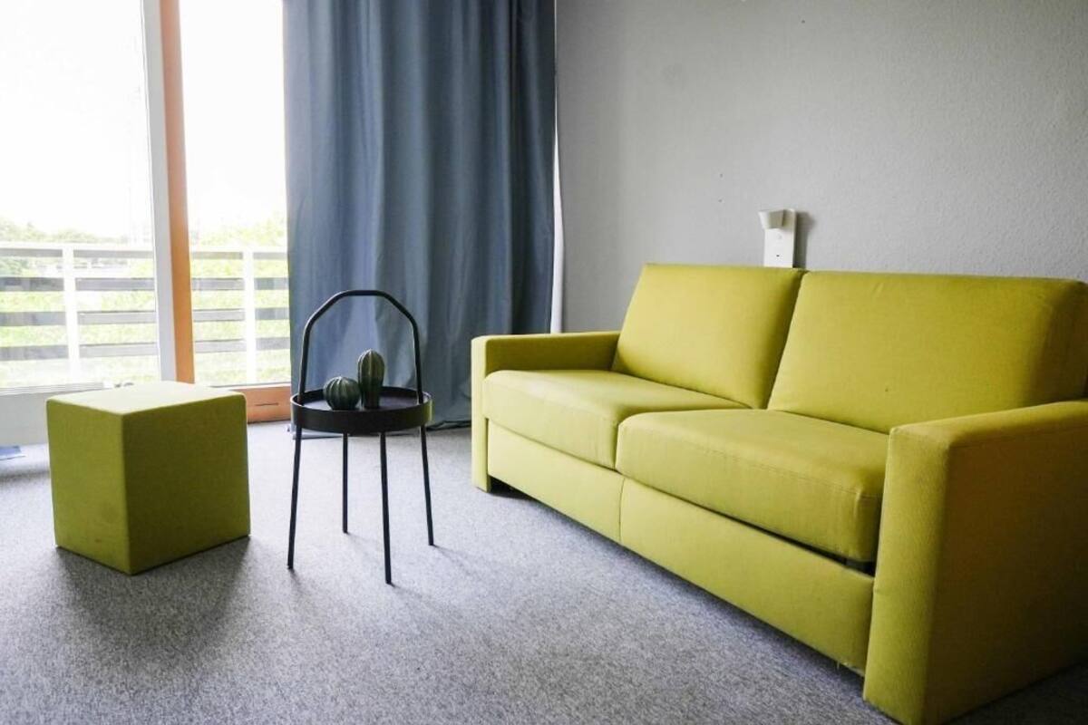 A living room with a yellow sofa, a small black table with a plant, and a window with curtains.
