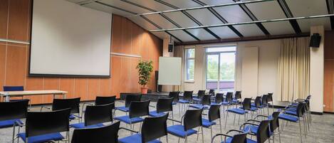 A conference room with rows of chairs, a projector screen, and a large window.