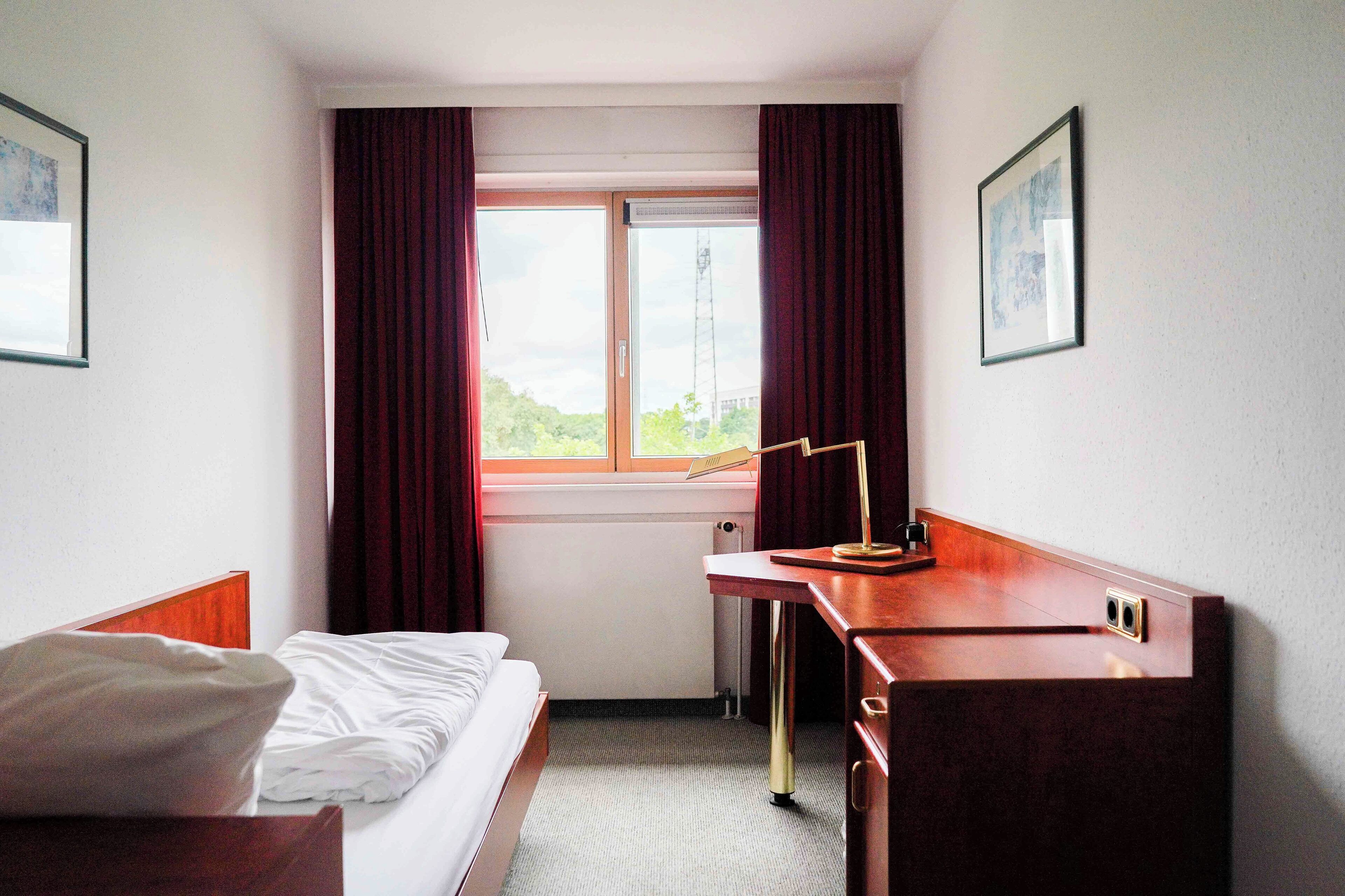A hotel room with a bed, a desk, and a window with curtains.