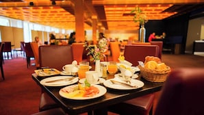 A breakfast setting with a table set for two, including plates of food, drinks, and a basket of bread.