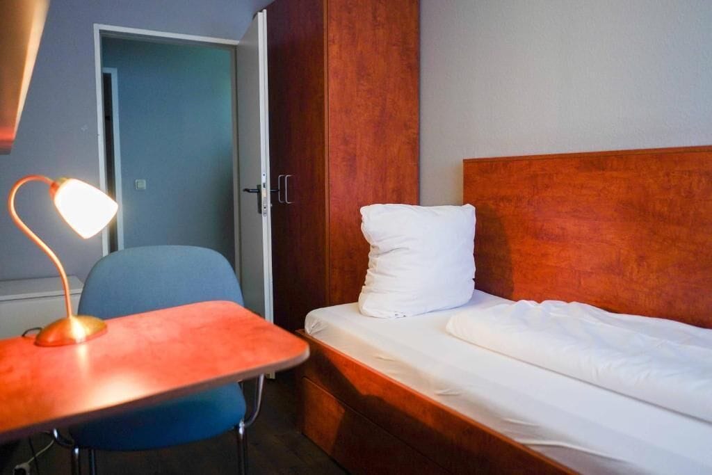 A hotel room with a bed, a desk with a lamp, and a chair.