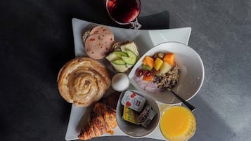 Un plateau de petit-déjeuner comprenant un croissant, du jambon, de l’avocat, des fruits, du granola, du yaourt et du jus d’orange.