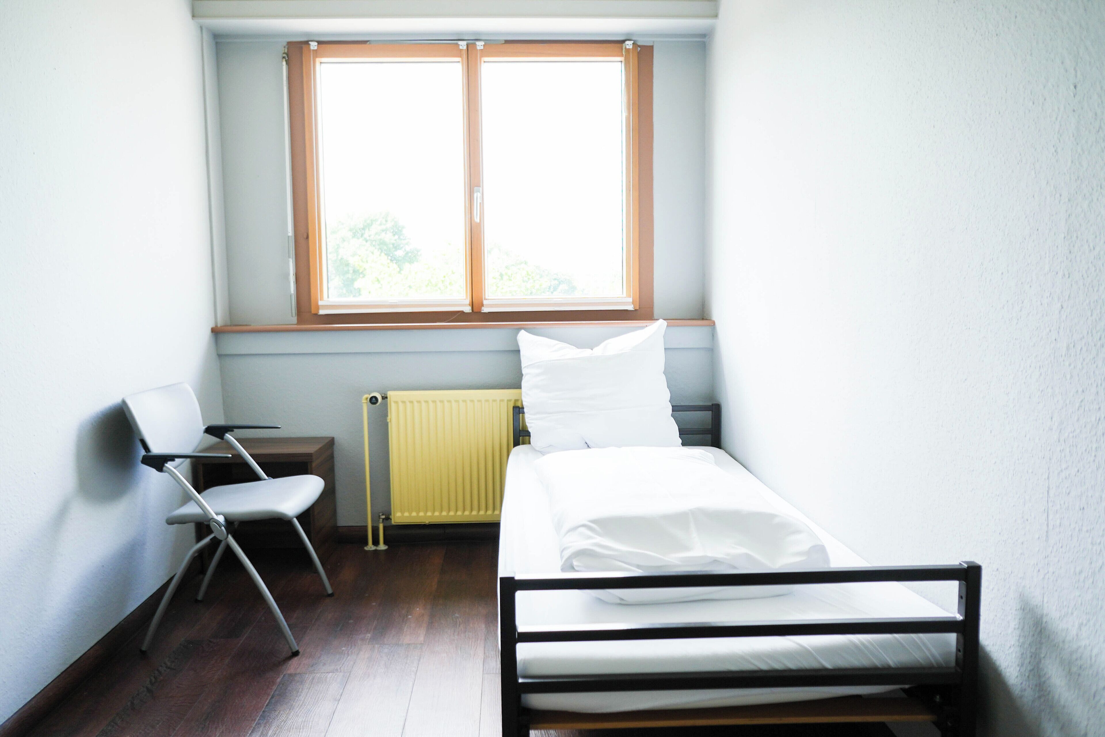 Et lille, rent værelse med en enkeltseng, en stol, en radiator og et vindue.
