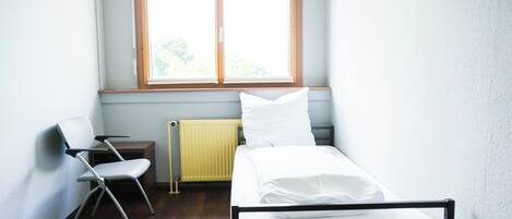 Et lille, rent værelse med en enkeltseng, en stol, en radiator og et vindue.