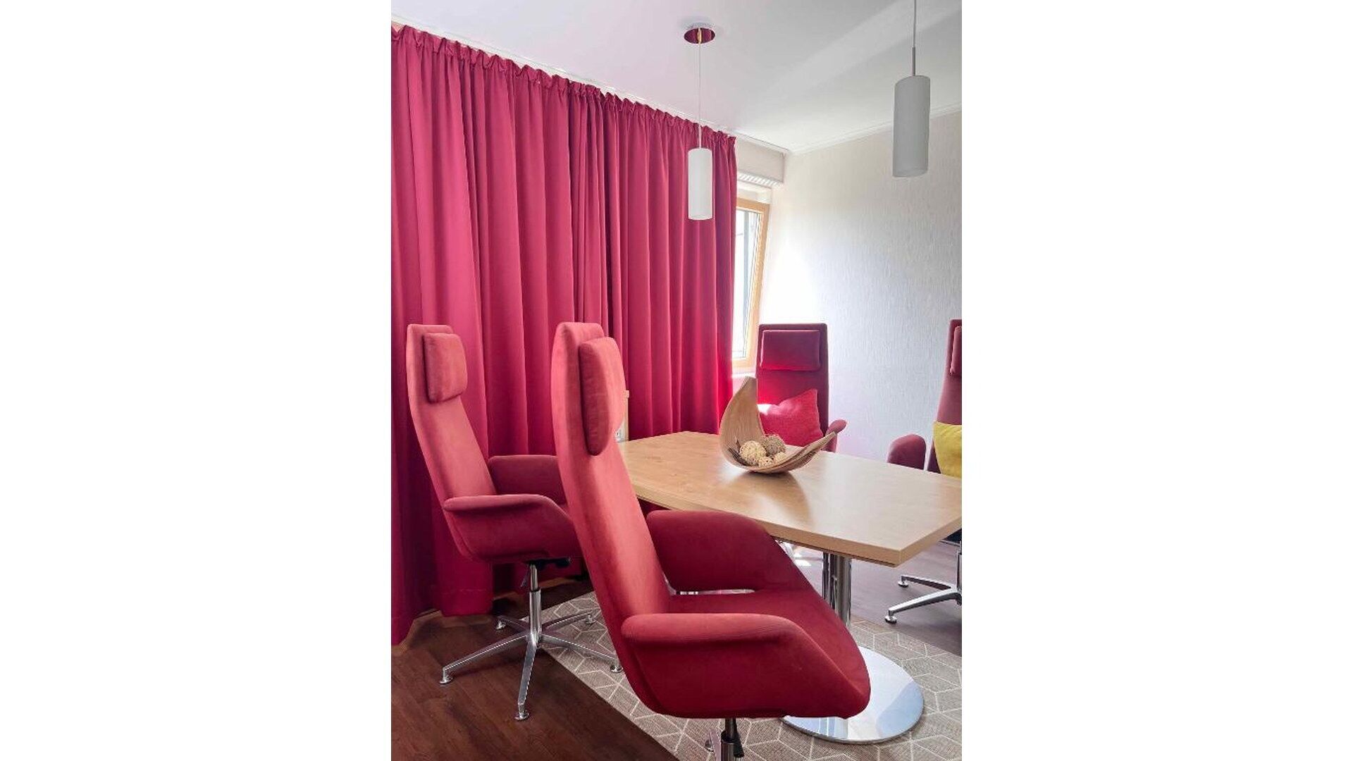 A conference room with a wooden table, two red chairs, and a red curtain.