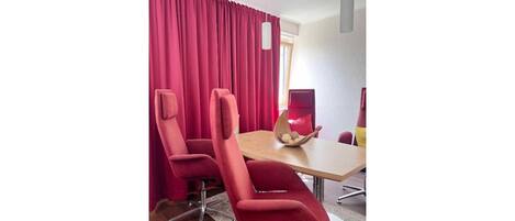 A conference room with a wooden table, two red chairs, and a red curtain.