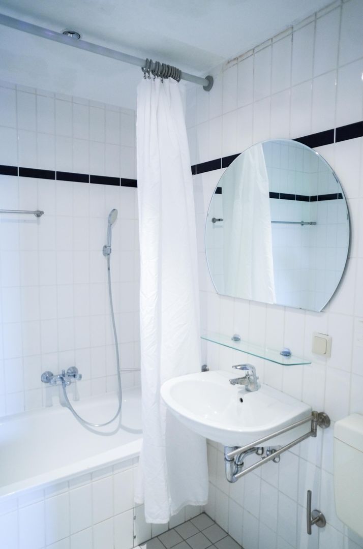 Une salle de bain avec une baignoire blanche, une douche, un lavabo avec une étagère en verre et un miroir rond.