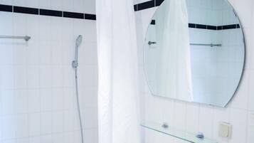 Une salle de bain avec une baignoire blanche, une douche, un lavabo avec une étagère en verre et un miroir rond.