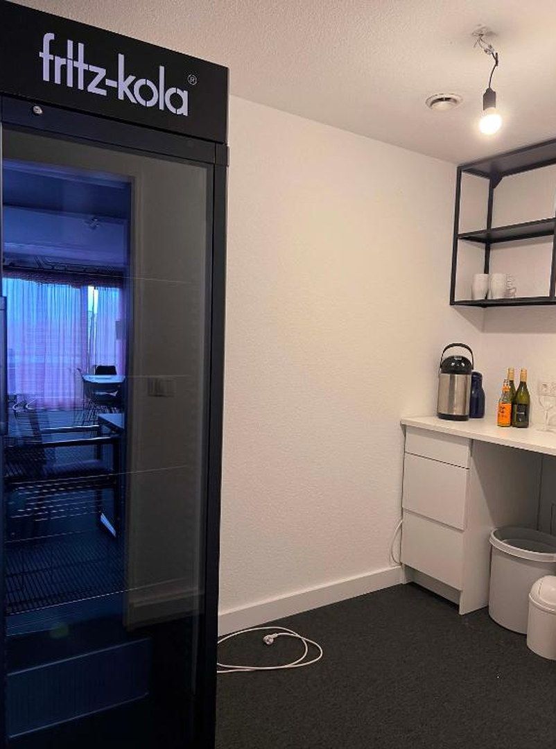 Una cocina moderna con puerta de vidrio de marco negro, un lavamanos, una encimera con botellas y un lámpara colgante.