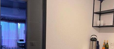 Une cuisine moderne avec une porte en verre à cadre noir, un évier, un plan de travail avec des bouteilles et un luminaire suspendu.