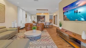 Una sala de estar moderna con un televisor grande, asientos cómodos, un comedor y una cocina al fondo.