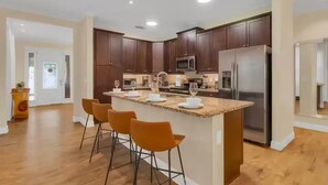 Una cocina moderna con armarios de madera oscura, una isla central con taburetes de bar, electrodomésticos de acero inoxidable y un amplio ventanal.