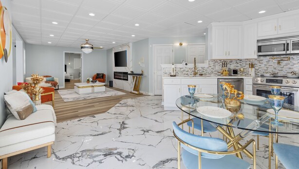 A modern kitchen with white cabinets, a marble floor, and a dining area with a glass table and blue chairs. - Stop the car! : Immediate Observation Required" (Manassas)