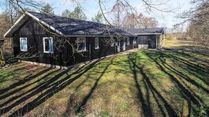 A large, single-story wooden building with a sloped roof, surrounded by a grassy area with shadows cast by trees. - 6 Person Holiday Park Home in Laeso (Læsø)