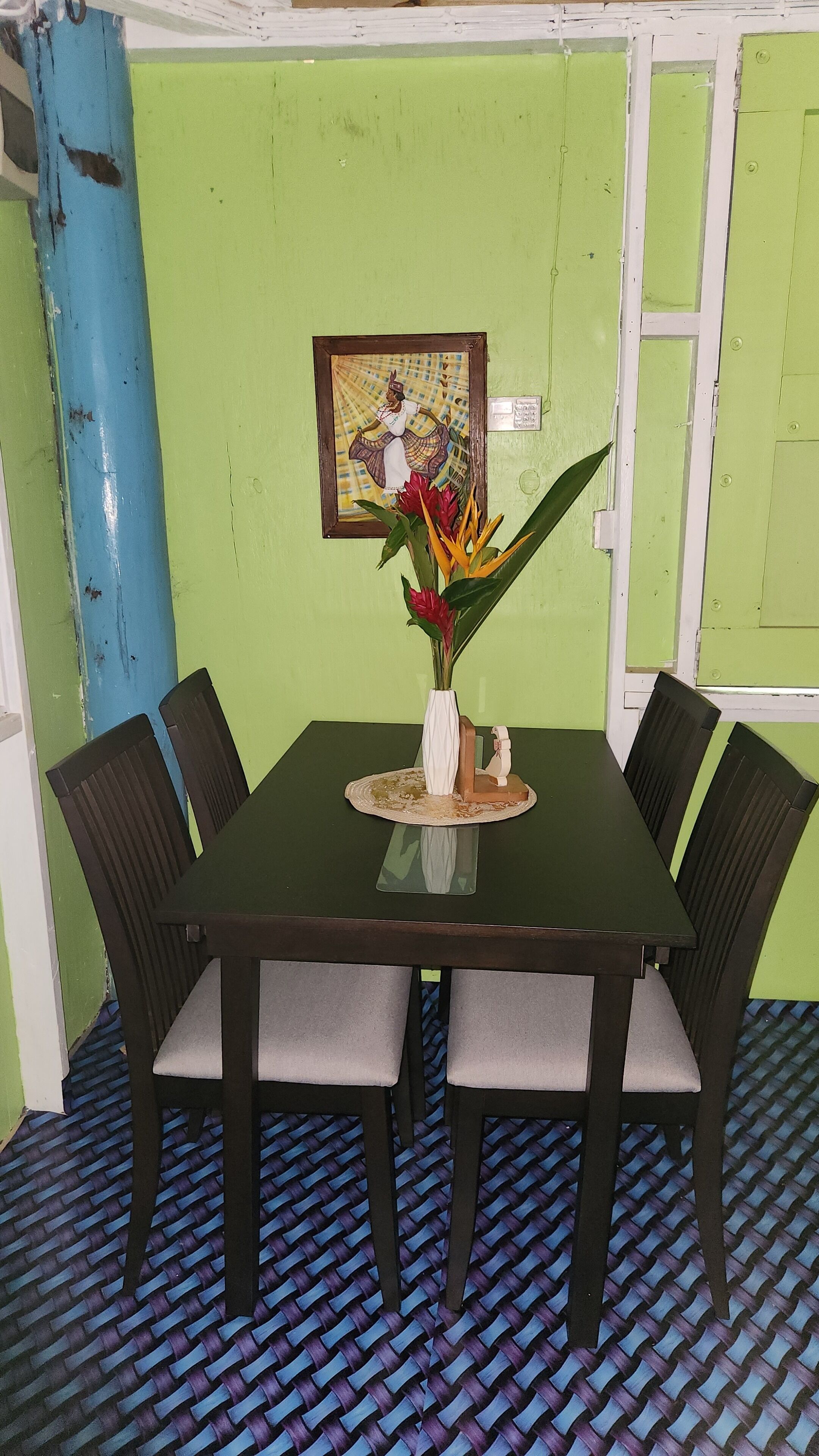 A dining table with four chairs, a vase with flowers, and a framed picture on the wall.