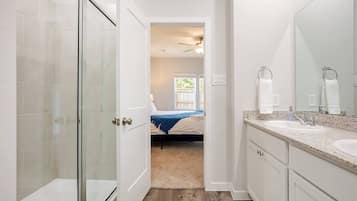 A modern bathroom with a glass shower door, a sink with a granite countertop, and a large mirror.