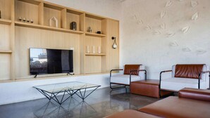 Una sala de estar moderna con un televisor de pantalla plana grande, sofás de cuero, una mesa de centro de vidrio y estanterías de madera con objetos decorativos.