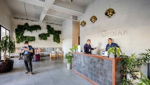 Un área de recepción con diseño moderno, que incluye un mostrador de recepción, plantas en macetas y un cartel en la pared.