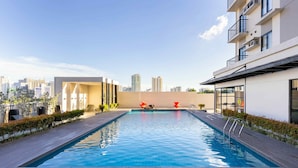 Una piscina en la azotea con vistas a un paisaje urbano, rodeada de edificios modernos y un cielo despejado.