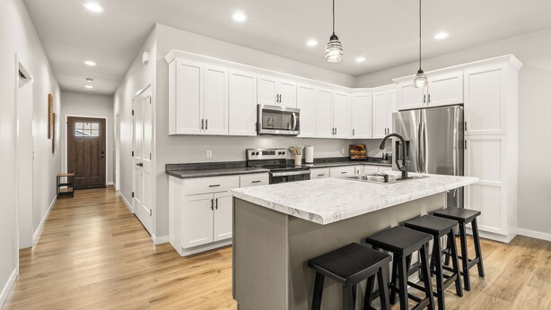 A modern kitchen with white cabinets, a large island with bar stools, stainless steel appliances, and a wooden floor. - Charming 3BR Plover Townhome w/ Modern Comfort, Amenities & Style (Plover)