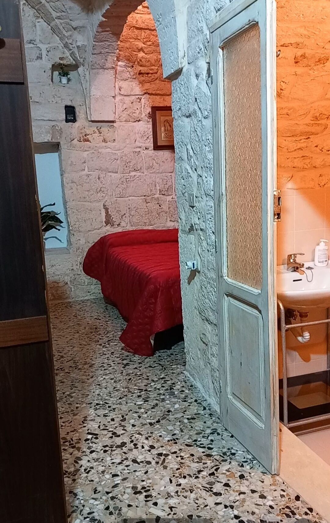 Una habitación con cama, lavamanos y puerta que da a otra estancia.