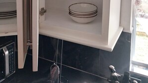 A kitchen cabinet with a microwave, a glass rack, and a window with a view of the outdoors. - Charming 2-bedroom apartment in Babonneau with WiFi, AC (Babonneau)